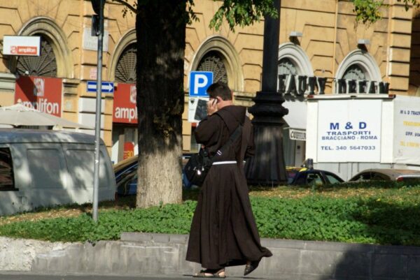 Priester met mobiel en laptop op straat.