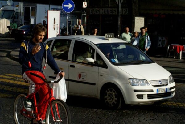 Fietser in drukke Romeinse straat, taxi op achtergrond.