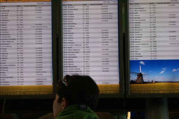 Gestrande reiziger kijkt wanhopig naar geannuleerde vluchten op Schiphol.