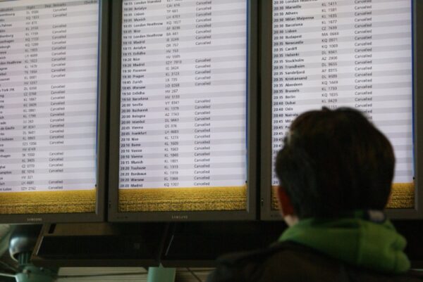 Gestrande reiziger kijkt wanhopig naar geannuleerde vluchten op Schiphol.