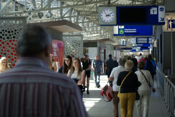 Treinreizigers in 's-Hertogenbosch, met informatieborden en klok.