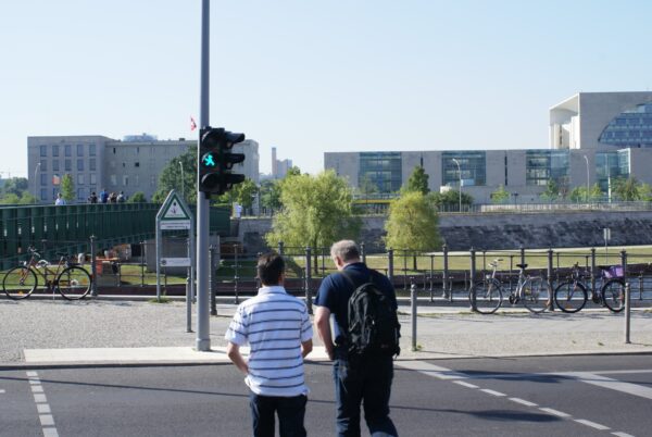 Mensen oversteken straat met Ampelm&auml;nnchen, Bondskanselarij op achtergrond.