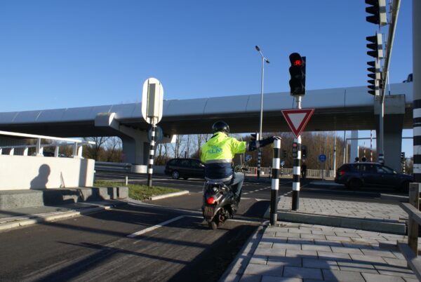 Scooterrijder met KLM-jas bij stoplicht Schiphol Oost.