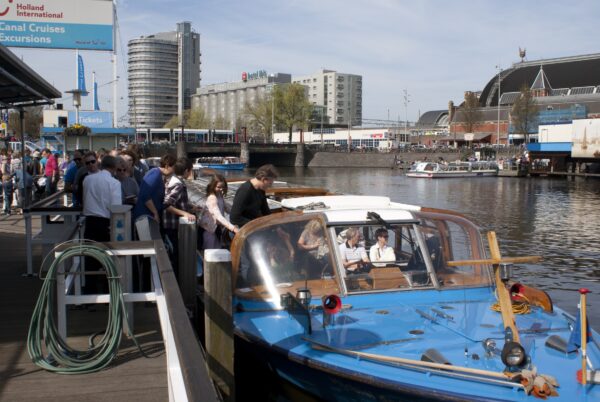 Toeristen stappen in bootje Holland International, Prins Hendrikkade, Amsterdam.