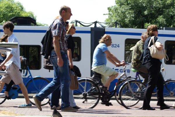 Voetgangers en fietsers over brug in Amsterdam, tram op achtergrond.