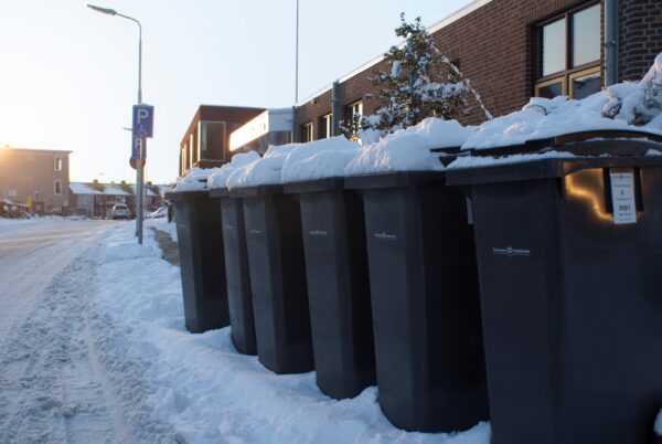 Vuilnisbakken in de sneeuw, klaar voor ophalen.